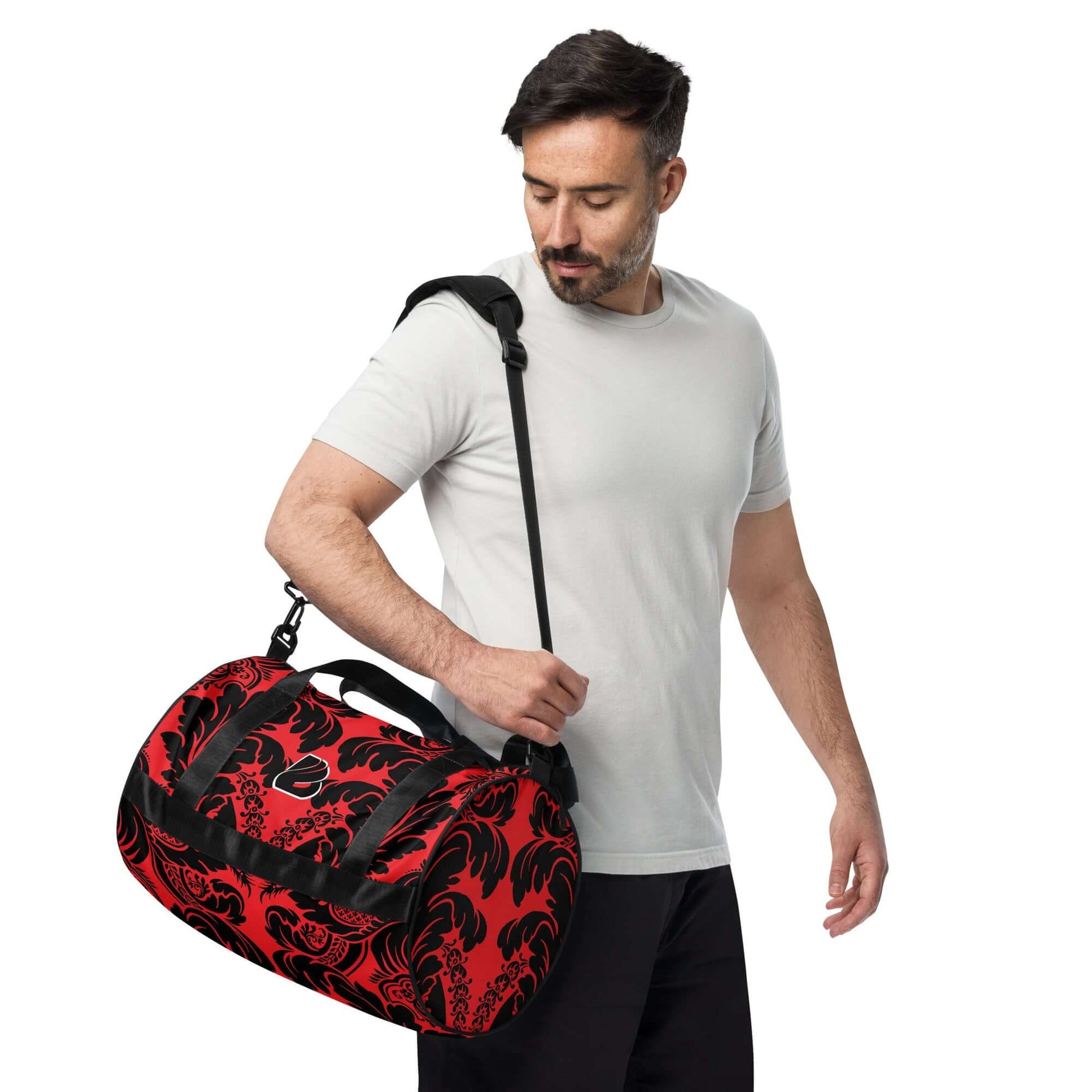 Man holding Allover-Print-Sporttasche N°5 in red with black pattern, showcasing durable and waterproof material, perfect for fitness.