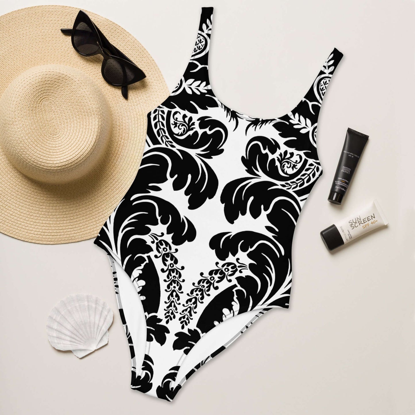 Einteiliger Badeanzug N°21 in floralen Schwarz-Weiß-Design, umgeben von Sommeraccessoires. Perfekt für Strand und Pool.
