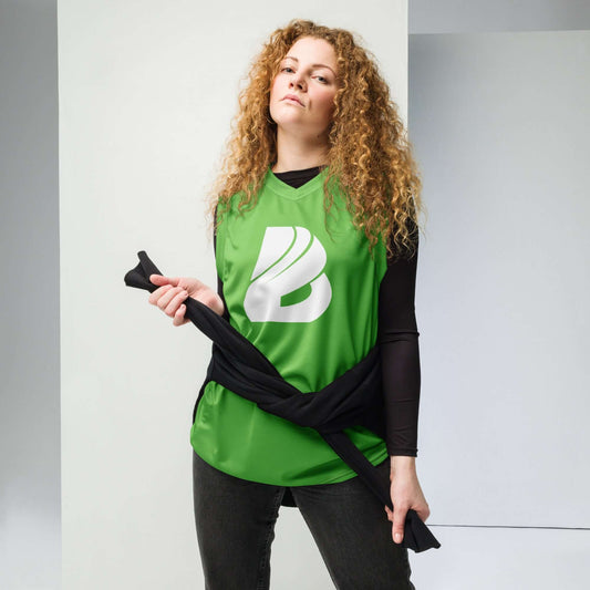 Person wearing Recyceltes Unisex-Basketballtrikot N°2 in green, styled with a black jacket and black pants, standing in a minimalist room.