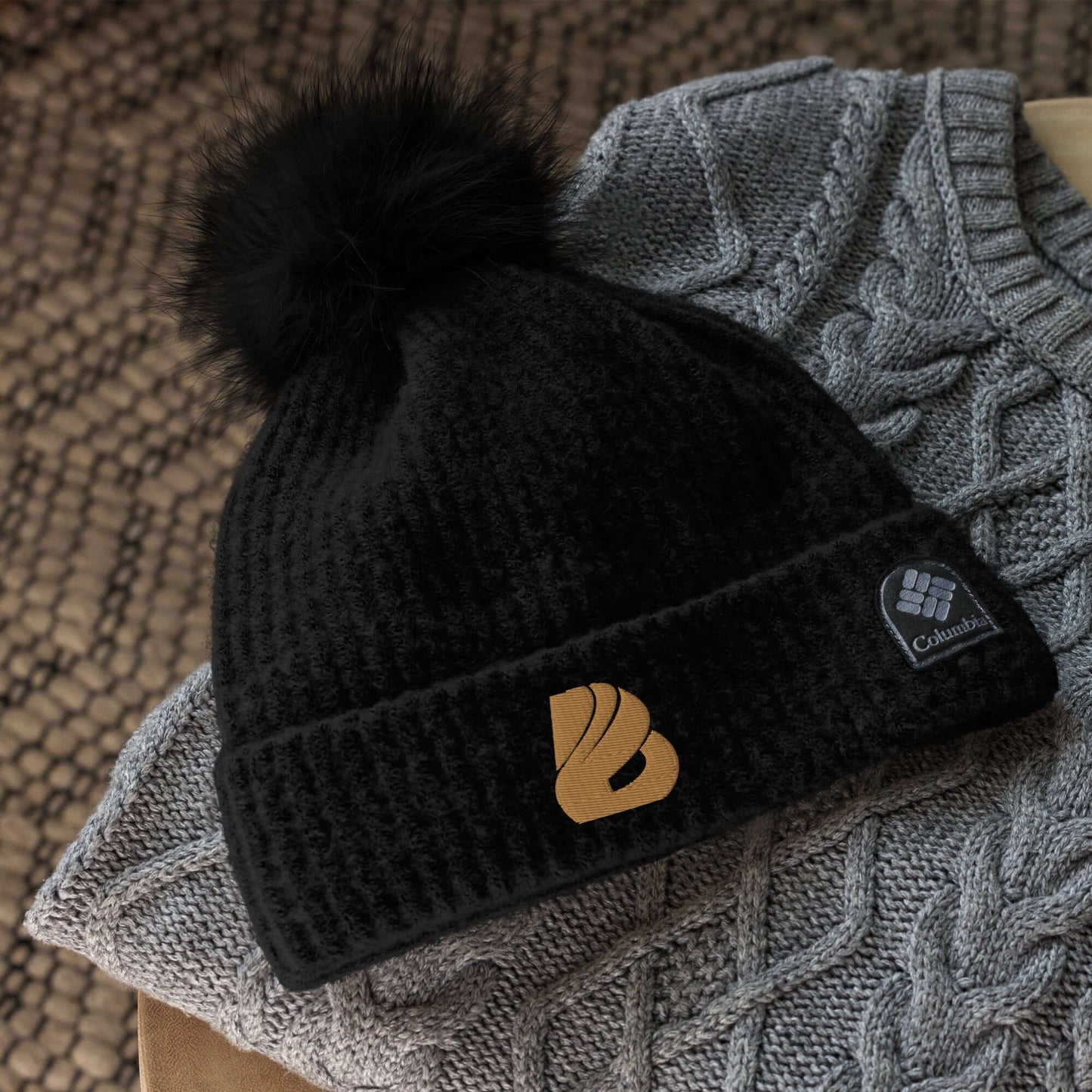 Columbia schwarze Bommelmütze mit goldenem Logo, kombiniert mit einem grauen Strickpullover.