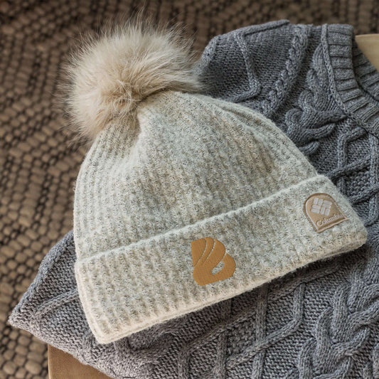 Alt Tag: Columbia Bommelmütze in beige on knitted background, featuring soft pom-pom and cozy fleece lining for winter fashion.
