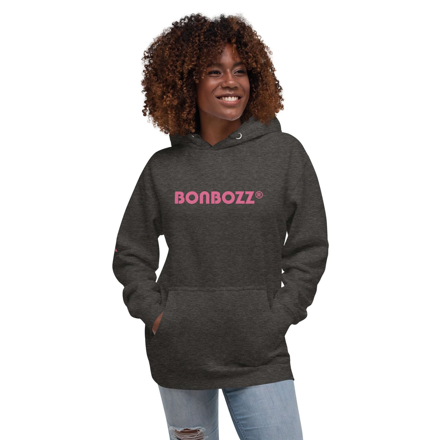 Smiling person wearing a dark gray Unisex-Kapuzenpullover with pink text print and front pocket.