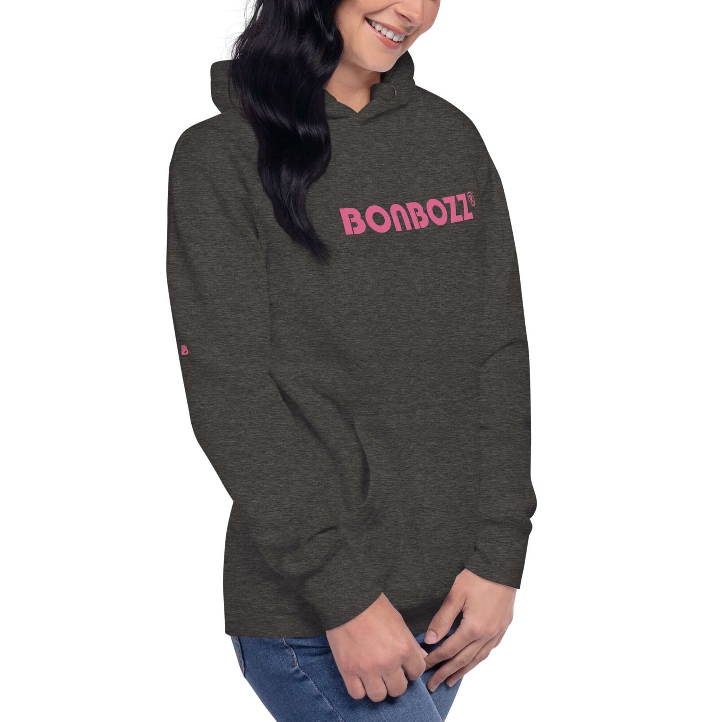 Unisex-Kapuzenpullover in charcoal gray featuring pink logo, worn by a smiling woman with hands clasped. Ideal for streetwear and comfort.