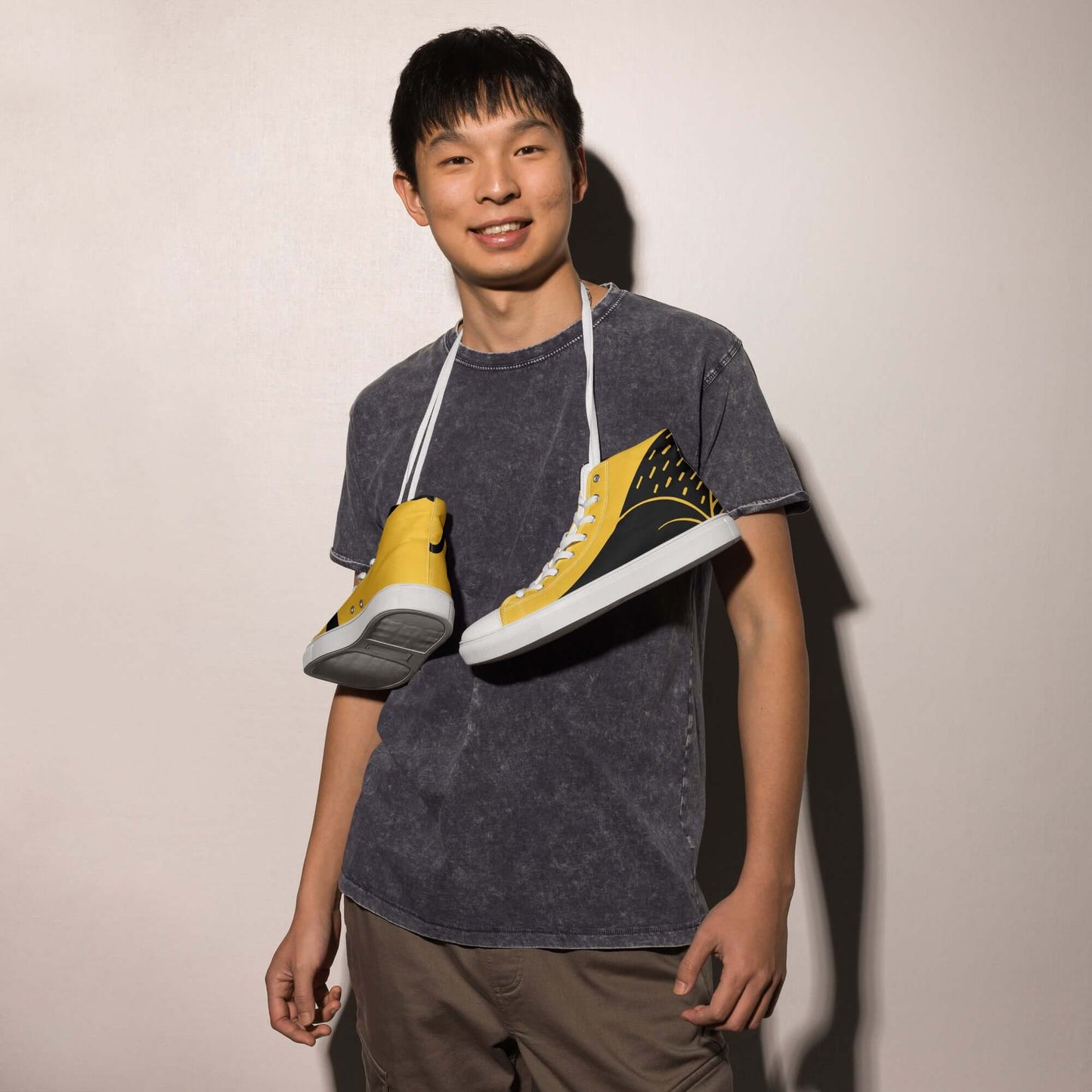 Young man holding High-Top Leinenschuhe für Herren N°8 with yellow and black design