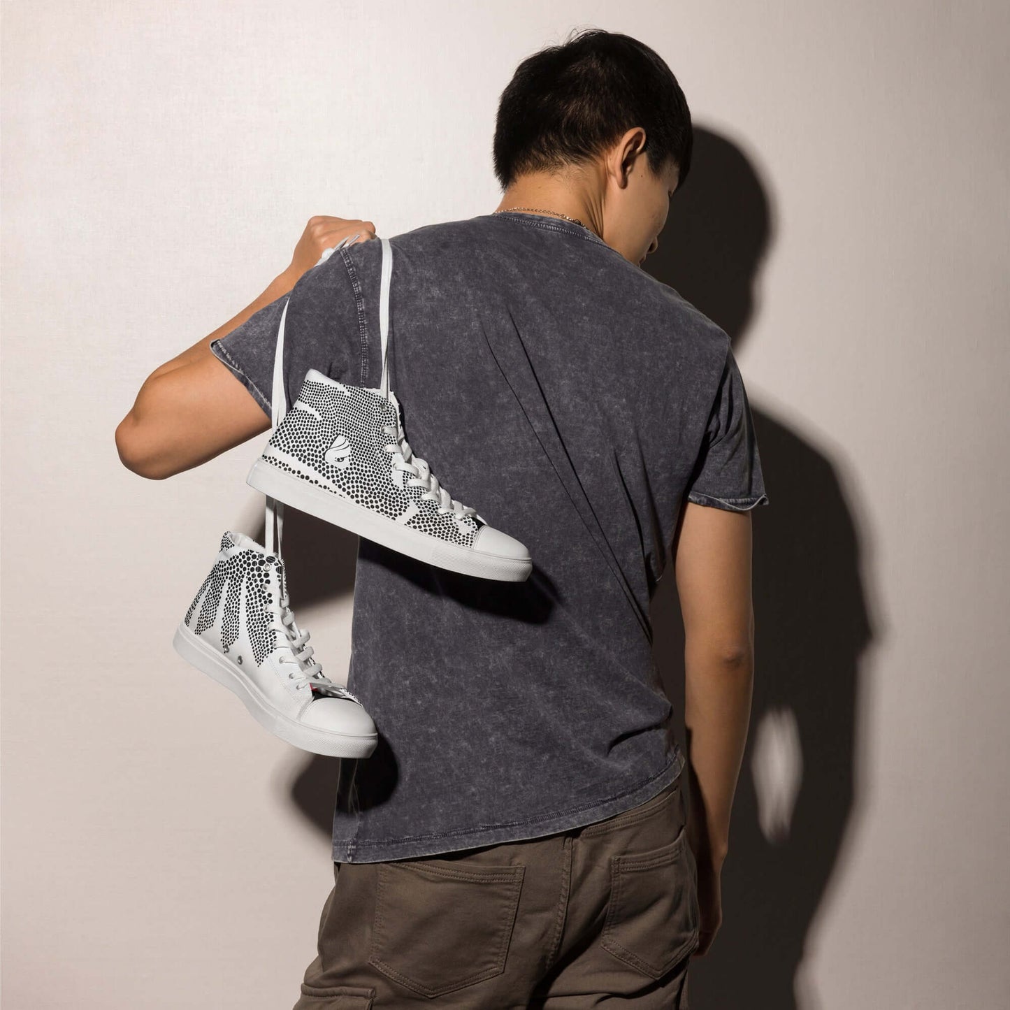 Person holding High-Top Leinenschuhe für Herren N°6 sneakers over shoulder, showcasing trendy design and style.