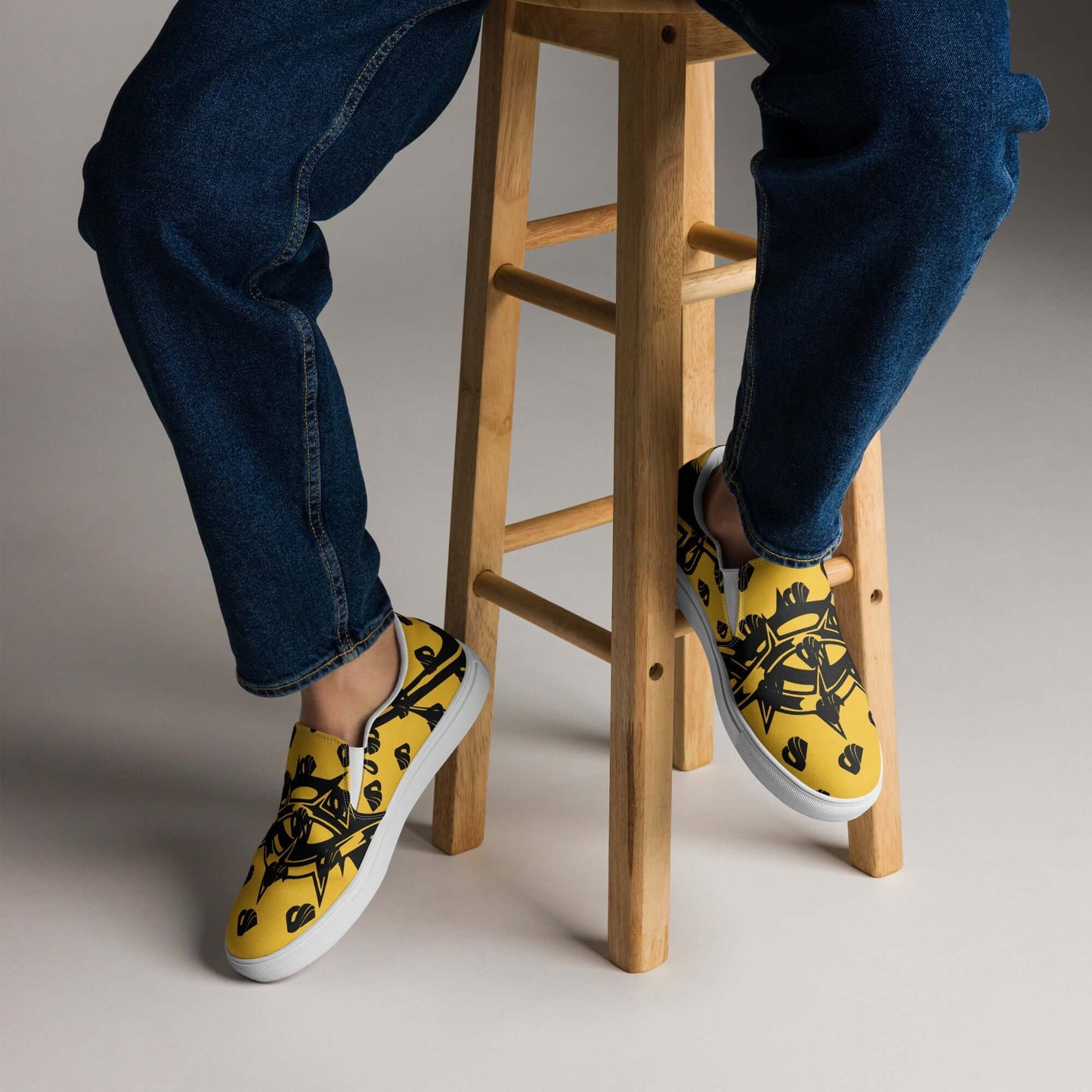 Person wearing Herren-Canvas-Slipper N°1 in yellow pattern, showcasing comfort and style with removable soft insoles on a wooden stool.