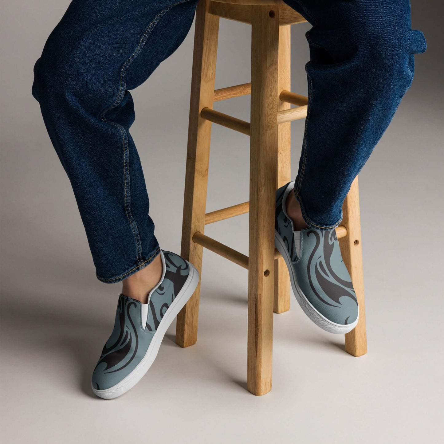 Person wearing Herren-Canvas-Slipper N°2 with denim jeans, featuring stylish design and comfort on a light wooden barstool.