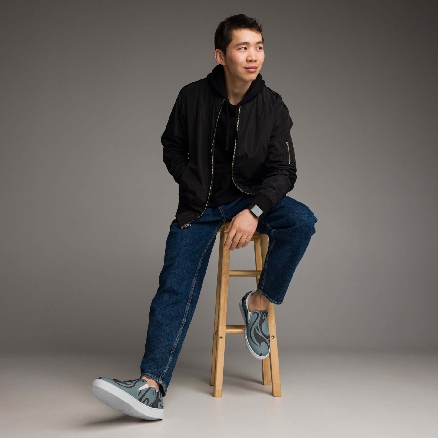 Man wearing Herren-Canvas-Slipper N°2, sitting stylishly on stool in casual outfit, showcasing comfort and modern design.