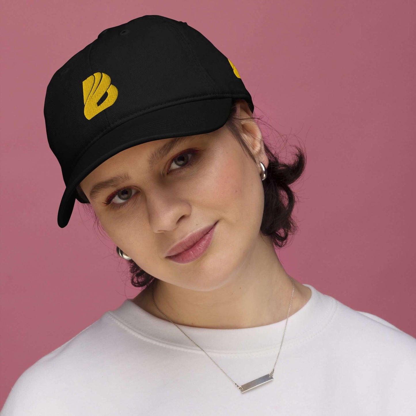 Person wearing Bio-Dad Hat N°1 made from 100% organic cotton, showcasing sustainable fashion with a black and yellow design on a pink background.