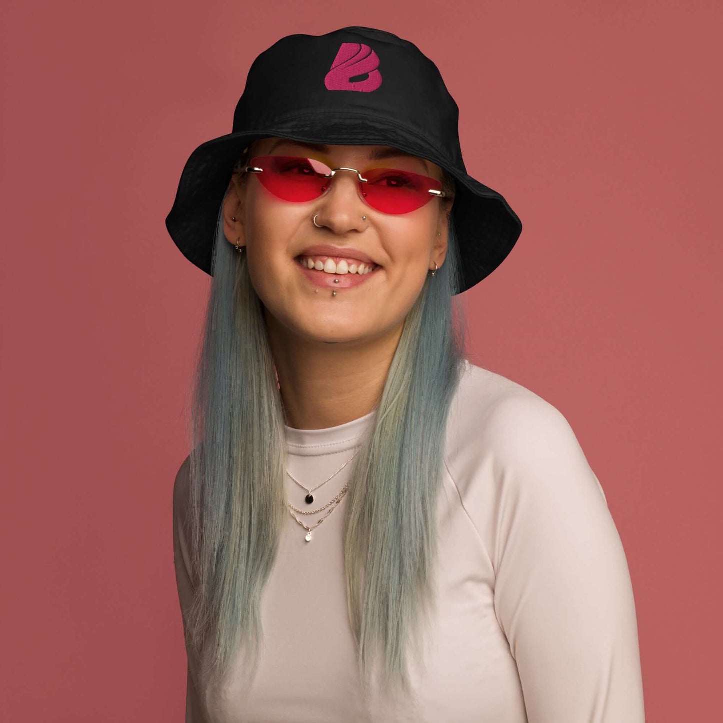 Person wearing Fischerhut aus Bio-Baumwoll-Twill N°1 in black with pink logo on a pink background, showcasing stylish and eco-friendly fashion.