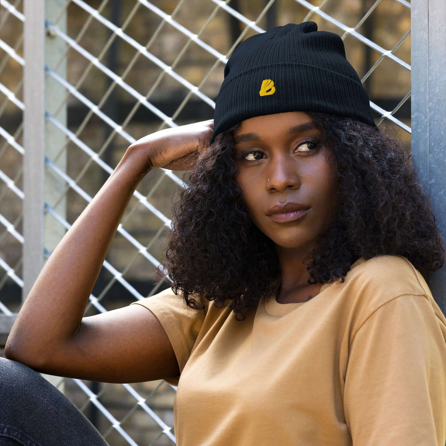 Woman wearing Gerippte Bio-Beanie in black with ribbed design, sitting by metal fence