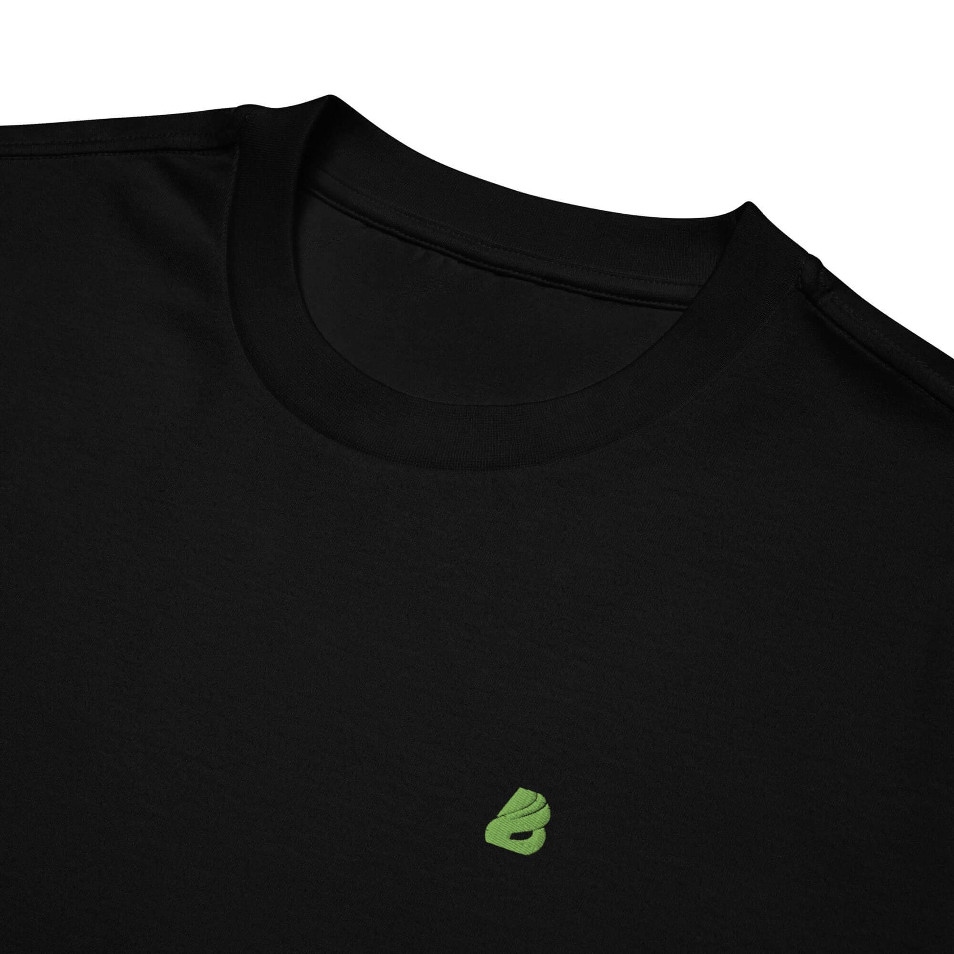 Schweres oversized T-Shirt aus Baumwolle, schwarzes Design mit kleinem grünen Logo darunter am Kragen für urbanen Streetwear-Look.