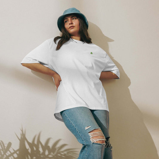 Woman wearing a white schweres oversized T-Shirt with blue jeans and a bucket hat, leaning against a wall.