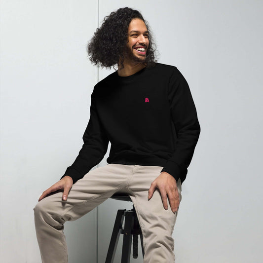 Man wearing Unisex Bio-Pullover in black, sitting on a stool.