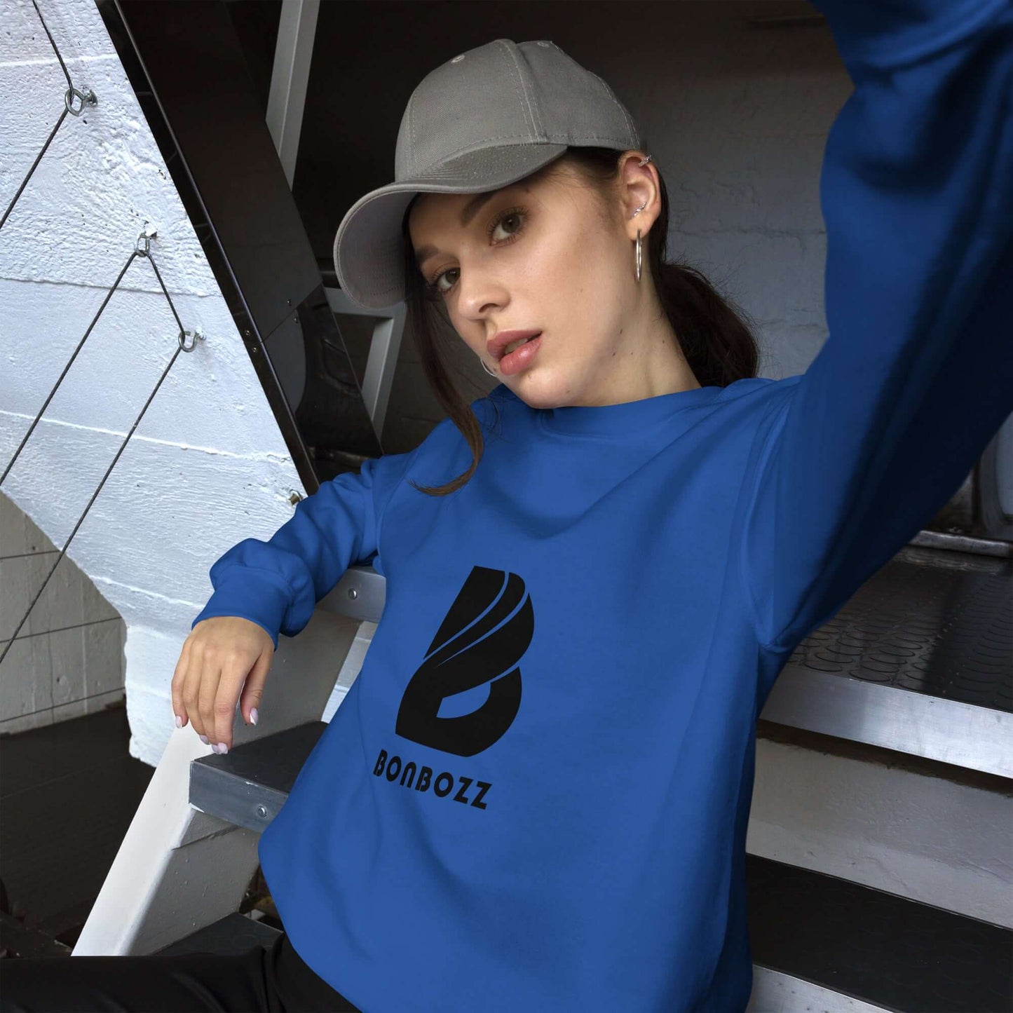 Person wearing a blue Unisex-Pullover sweatshirt, sitting casually on stairs indoors, showcasing comfortable and stylish design.