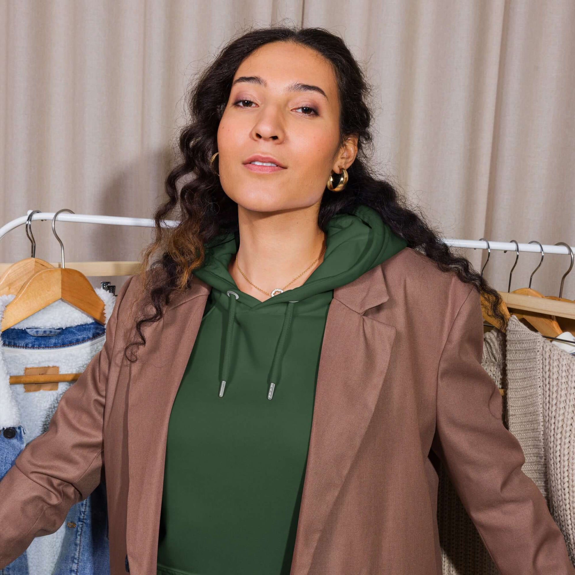 Woman in blazer wearing Unisex Bio-Raglan-Hoodie standing by clothing rack.