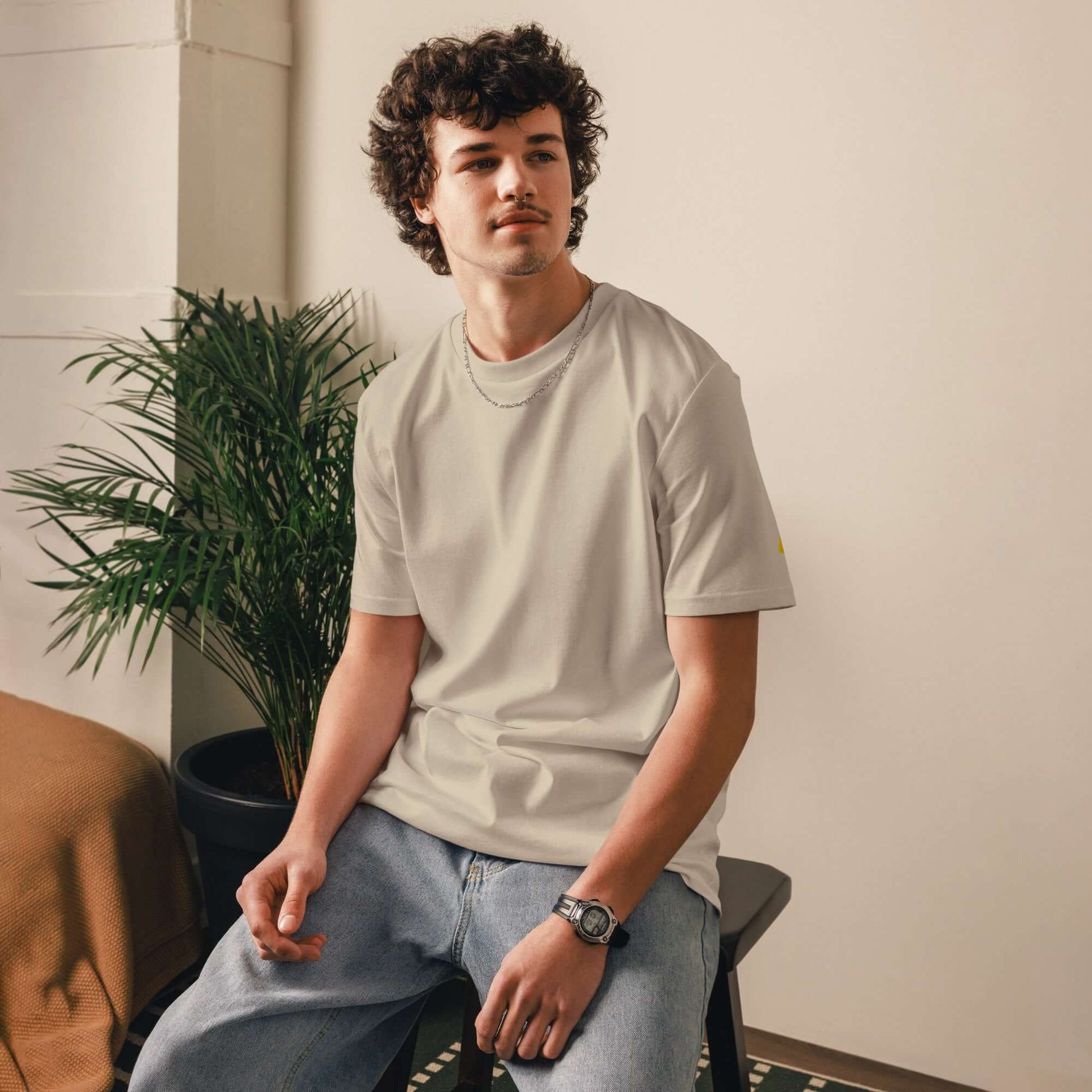 Person wearing Unisex-Bio-Baumwoll-T-Shirt in a room with plants, showcasing sustainable fashion.