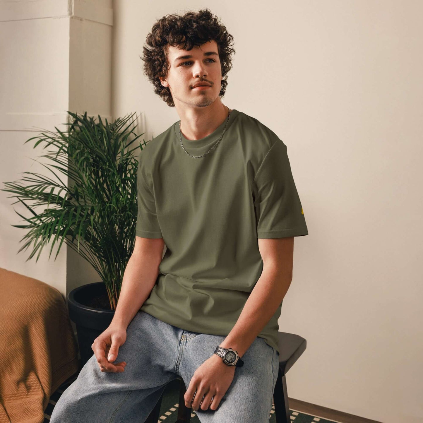 Person wearing an olive green Unisex-Bio-Baumwoll-T-Shirt in a stylish indoor setting