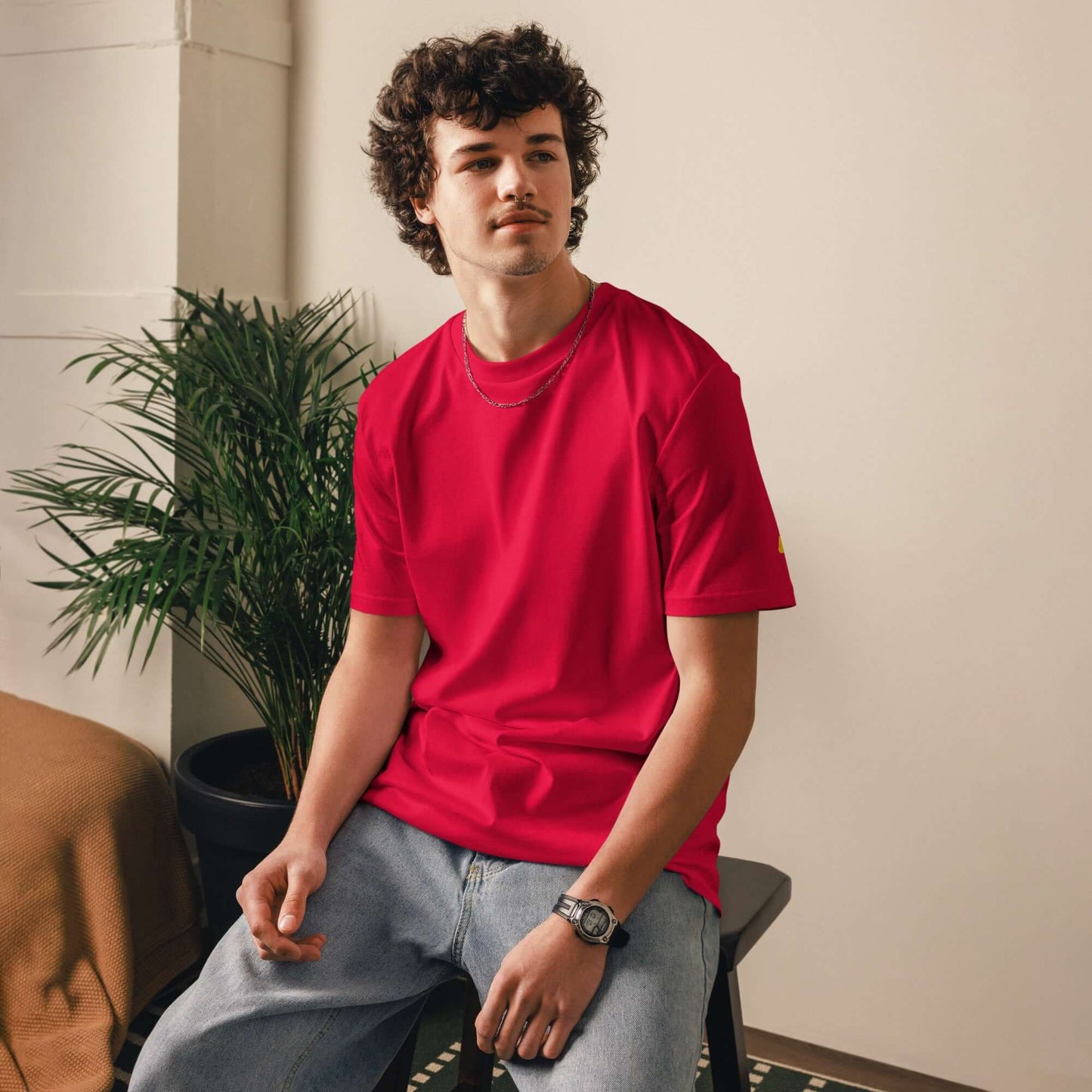 Person wearing Unisex-Bio-Baumwoll-T-Shirt in vibrant red color, casually sitting on a chair, showcasing sustainable fashion.