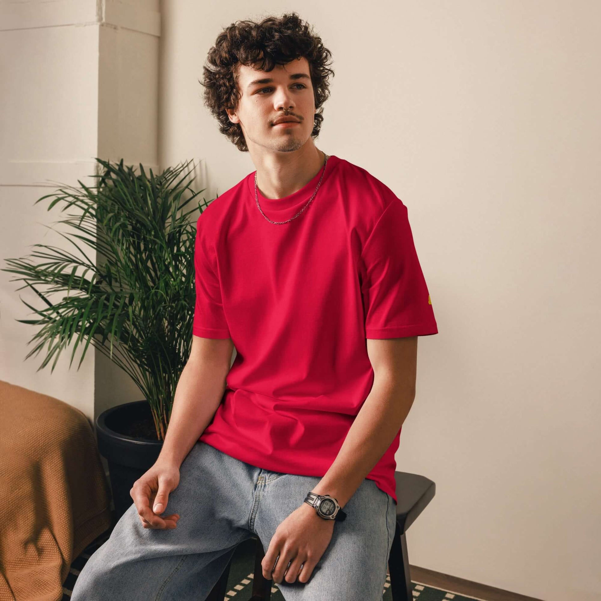 Person wearing Unisex-Bio-Baumwoll-T-Shirt in vibrant red color, casually sitting on a chair, showcasing sustainable fashion.