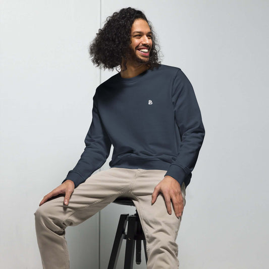 Model wearing Unisex Bio-Pullover N°0 in dark blue, sitting on a stool, showcasing the eco-friendly design with soft materials and relaxed fit.