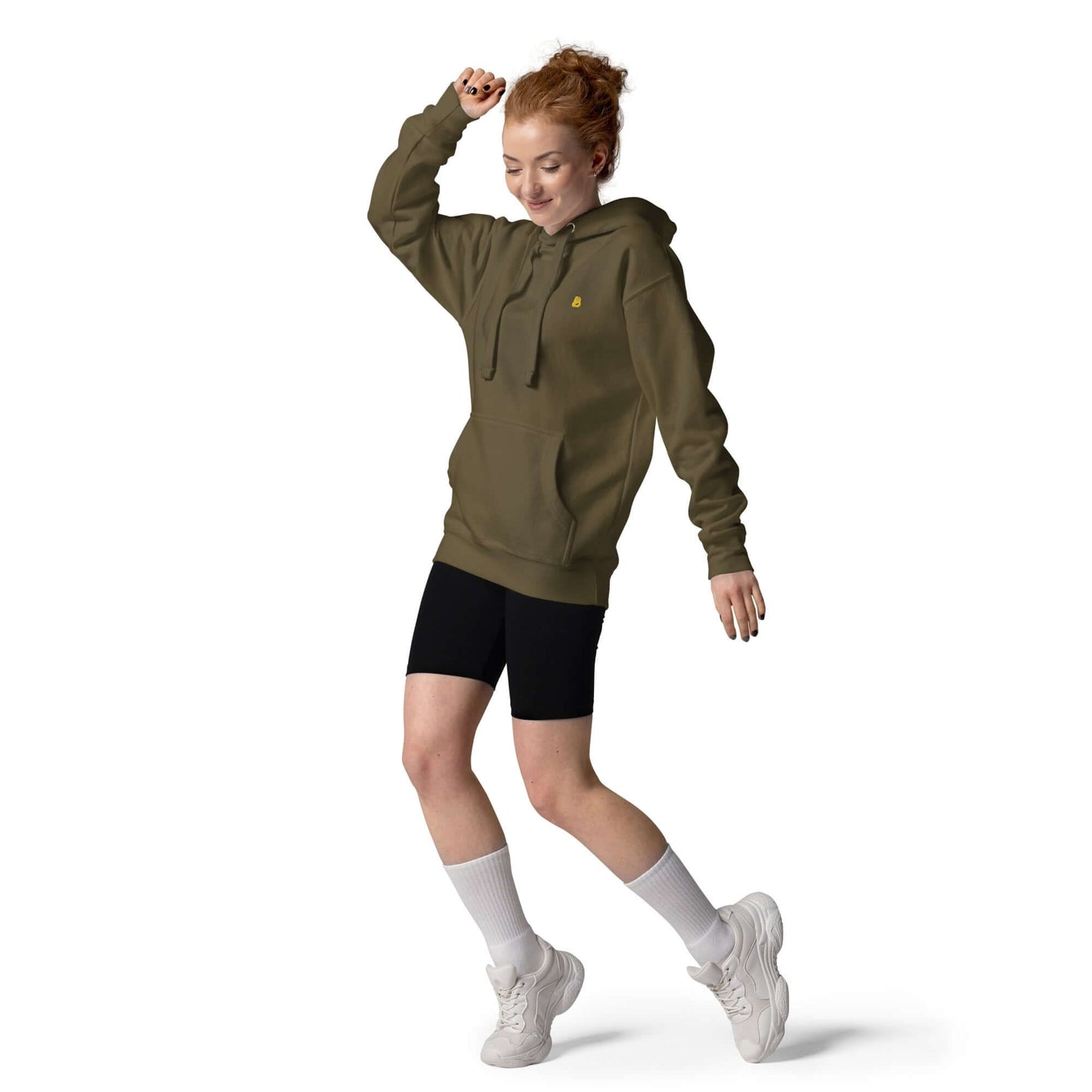 Person wearing an olive green Unisex-Kapuzenpullover N°50 with black shorts, white socks, and sneakers, posing playfully against a white background.