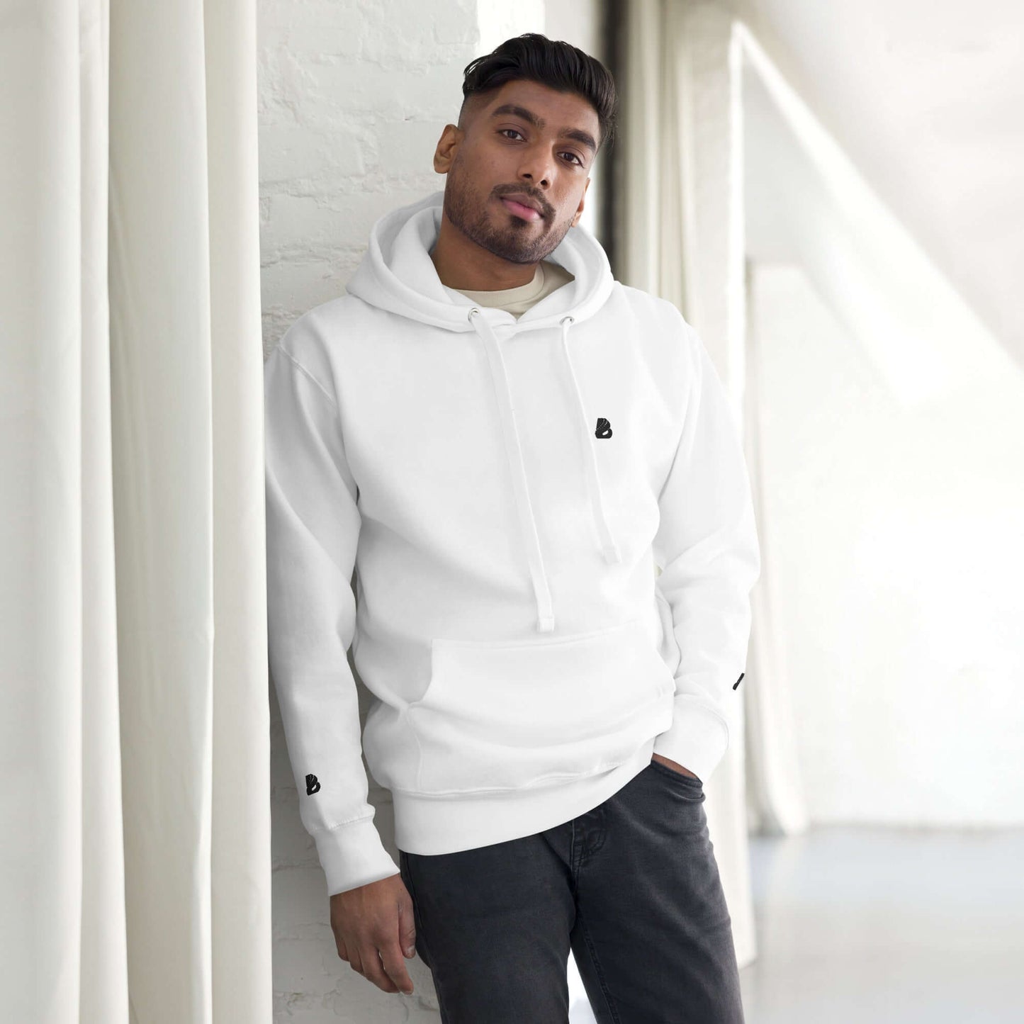 Person wearing Unisex-Kapuzenpullover N°49, white hoodie with front pocket and warm hood indoors, showcasing streetwear style.