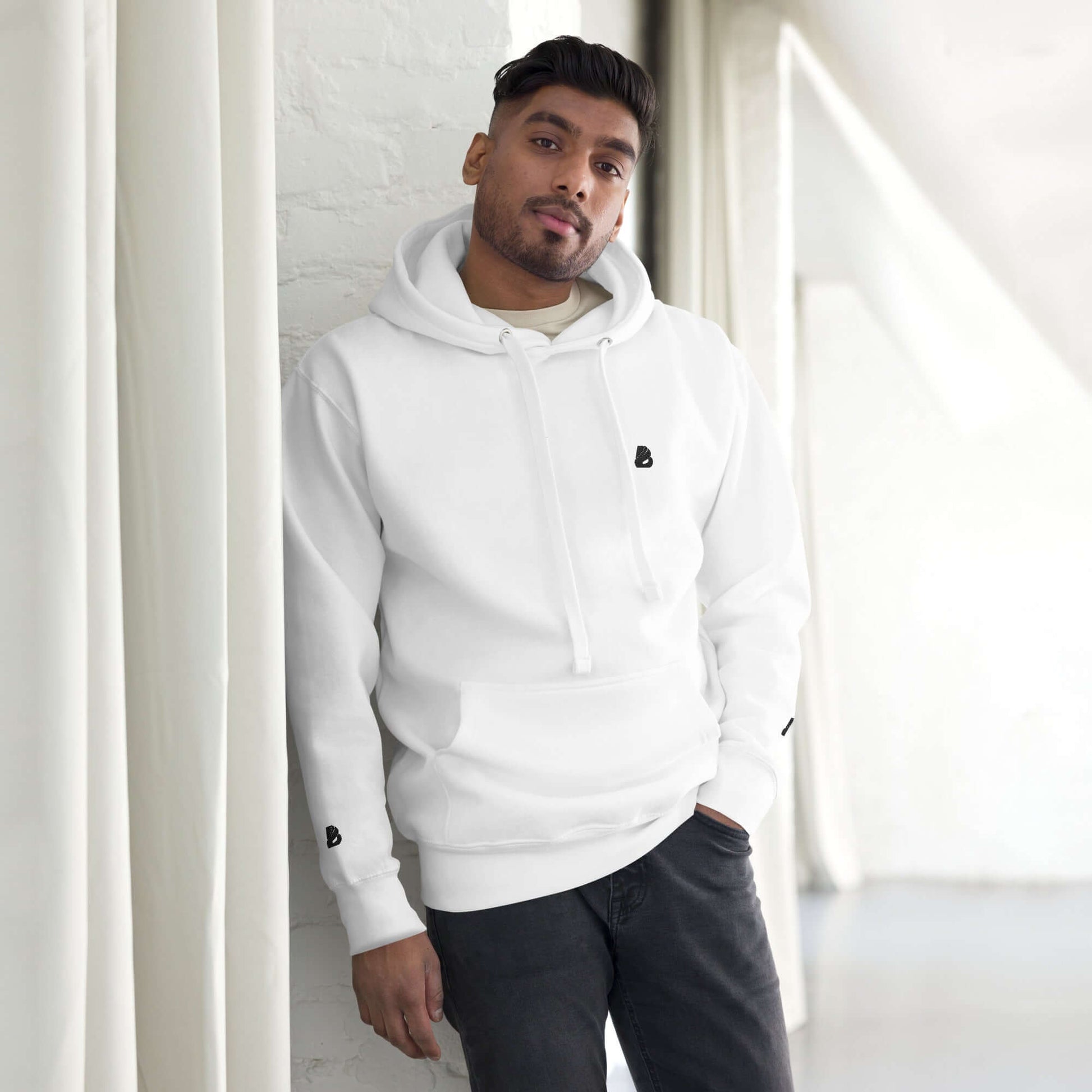 Person wearing Unisex-Kapuzenpullover N°49, white hoodie with front pocket and warm hood indoors, showcasing streetwear style.