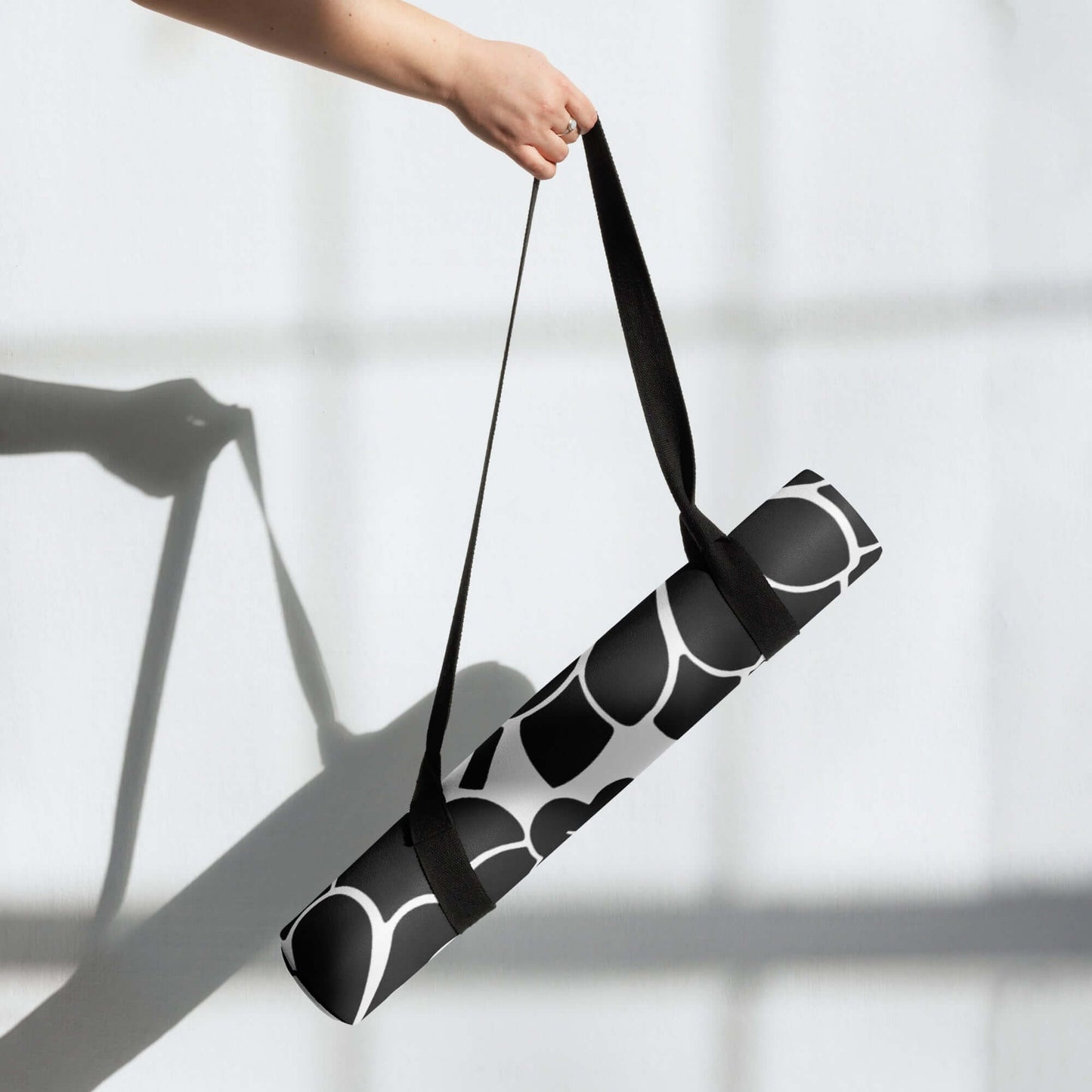 Person holding a rolled Yoga-Matte N°0 with stylish design and carrying strap against a bright background.