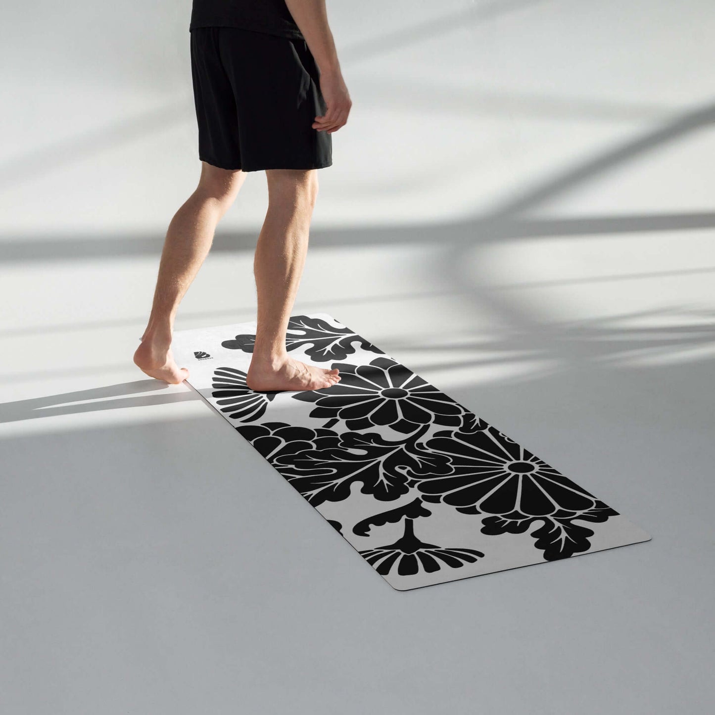 Person standing on Yoga-Matte N°0 with black floral design, rubber base, and microvelours top, ideal for yoga, stretching, meditation.