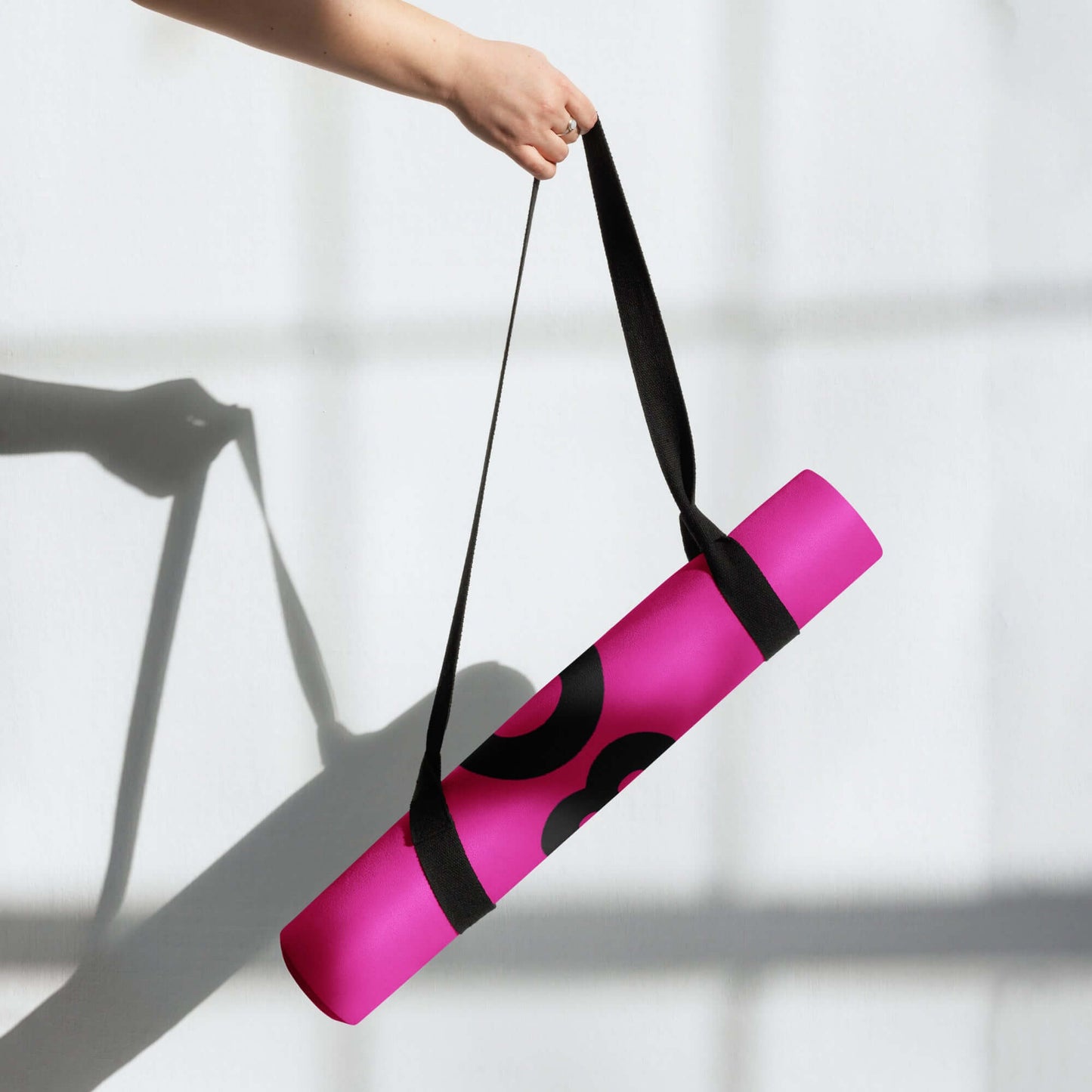 A person holding the pink Yoga-Matte N°1 with a black strap, showcasing its portability and chic design.