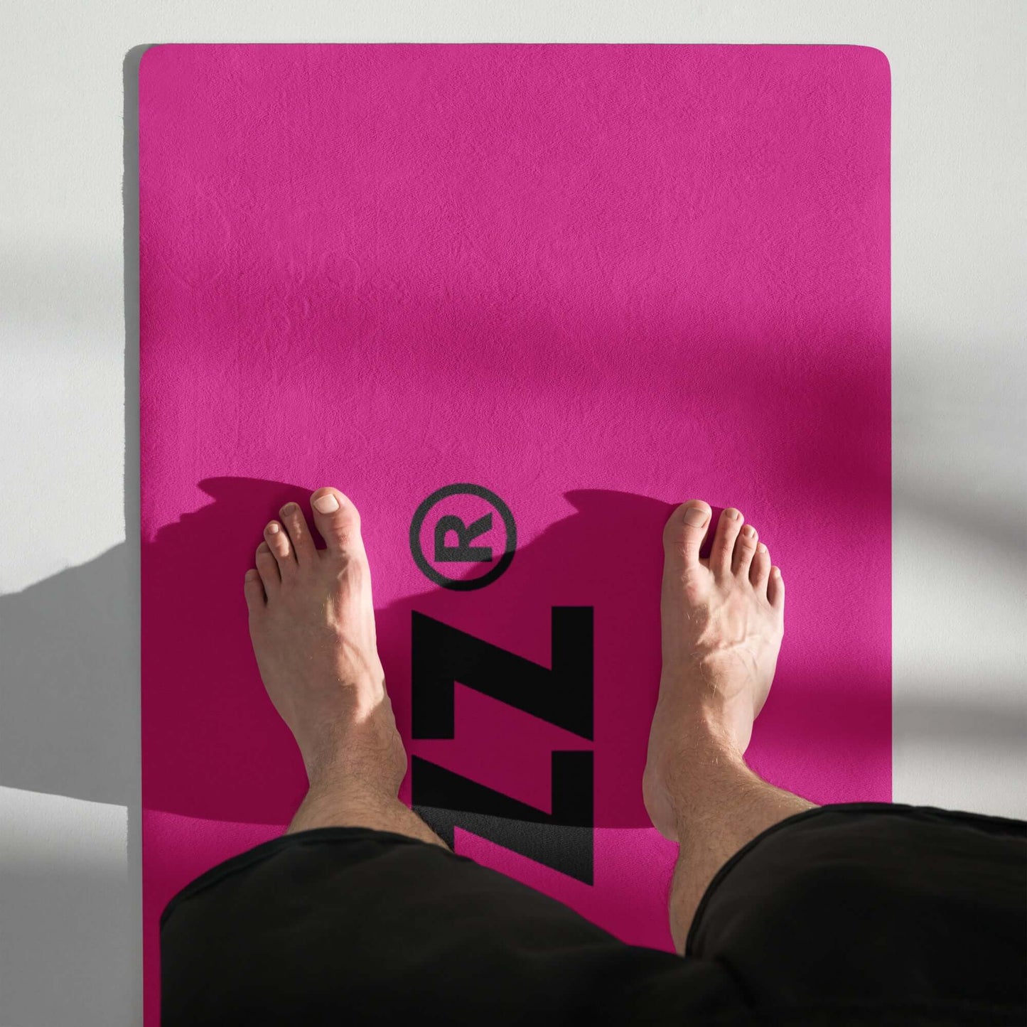 Person standing on pink Yoga-Matte N°1 with black logo, featuring non-slip rubber back and microsuede top for stability and comfort.