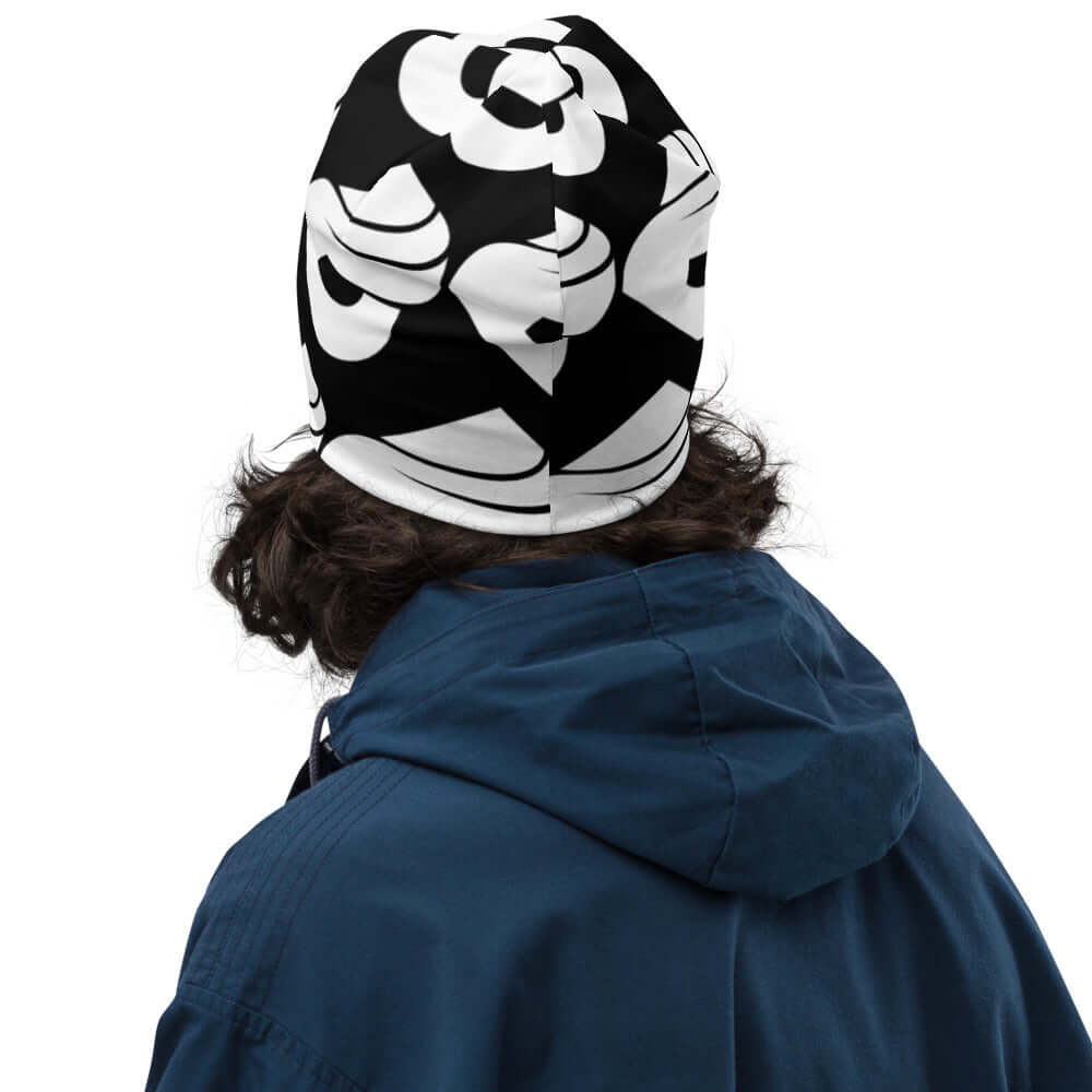 Warm and stylish Allover-Beanie N°0 with black and white pattern, perfect for cold days, shown on a person with curly hair and blue jacket.