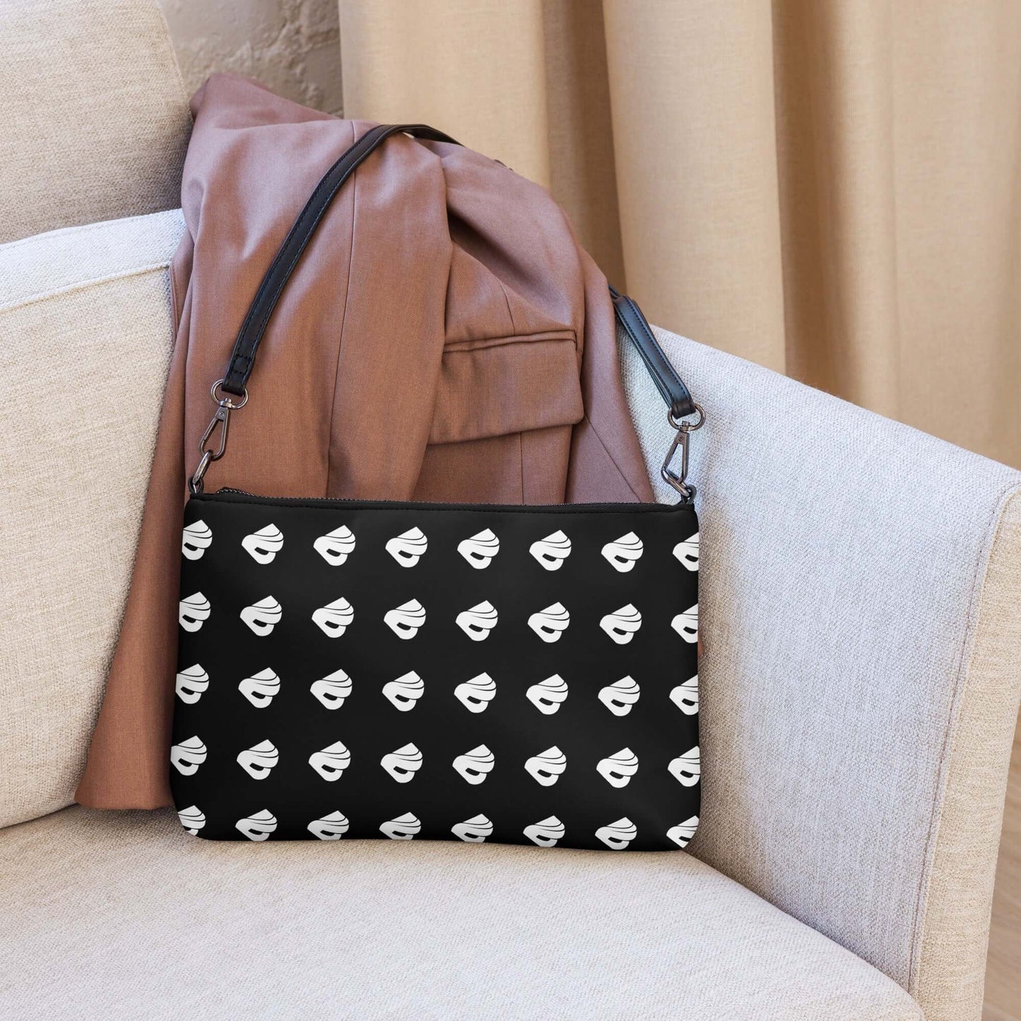 Umhängetasche N°0 in black with white pattern, displayed on a beige sofa with a brown coat.