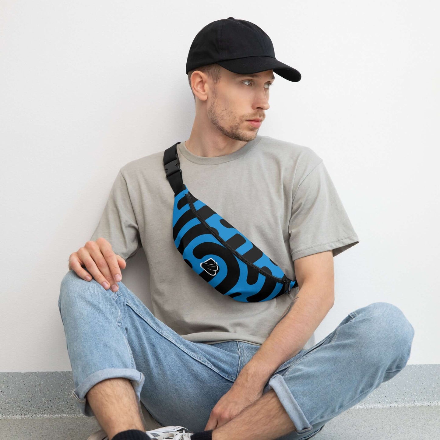 Stylish man wearing a blue and black Gürteltasche N°27 fanny pack, seated on the floor in casual attire.