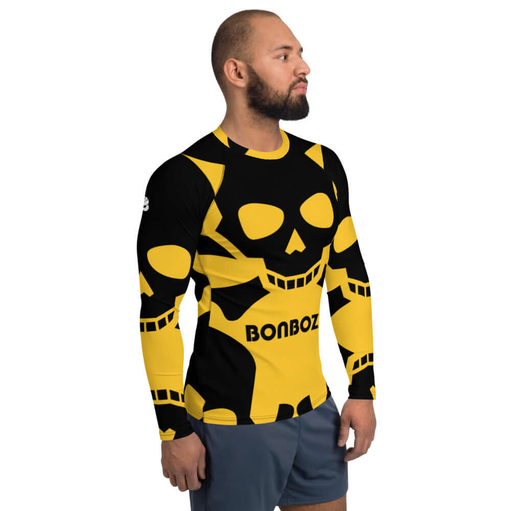 Man wearing Herren-Rash-Guard N°8 in black and yellow with skull design, sporty and protective long-sleeve top for outdoor activities.
