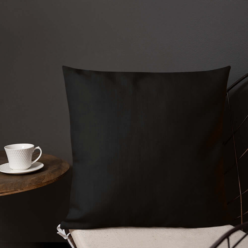 Premium-Kissen N°0 in elegantem Schwarz auf einem Stuhl, neben einer Tasse Kaffee auf einem Tisch, luxuriös und stilvoll.