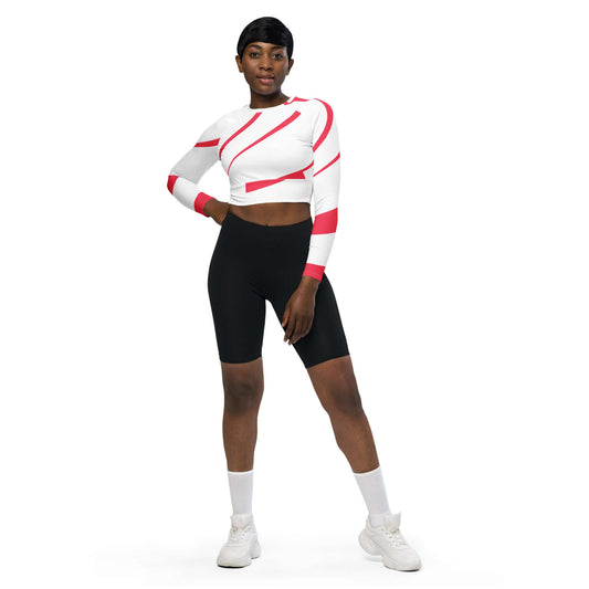 Model wearing Recyceltes Langarm Crop Top mit Allover-Druck N°1 in white with red design, paired with black shorts and white sneakers.