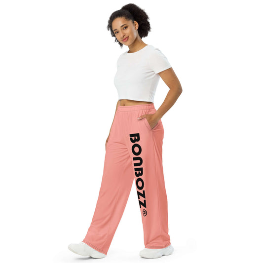 Woman wearing Unisex-Hose mit weiten Beinen und Allover-Druck N°0, pink with 'BONBOZZ' text, side pockets, white crop top, casual style