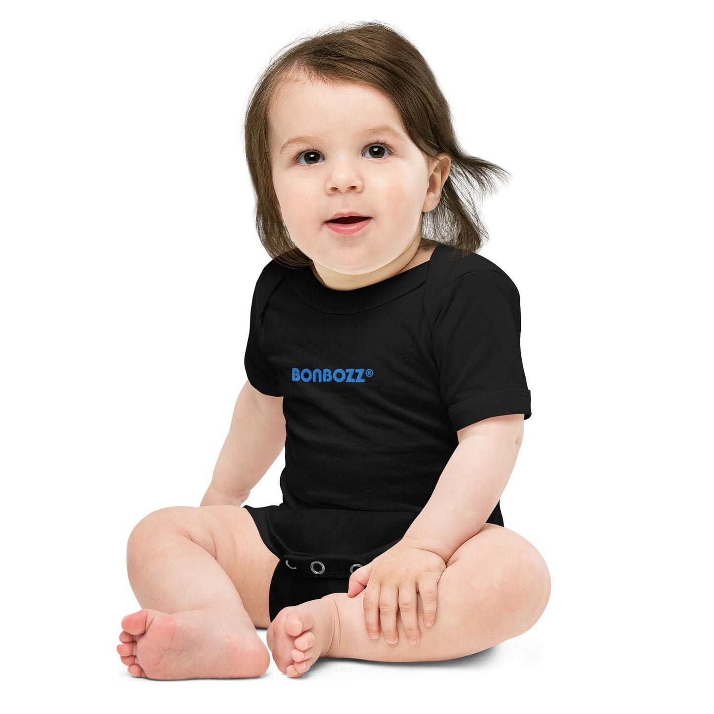Baby wearing Kurzärmliger Baby-Einteiler N°0 in black sitting on floor, showcasing comfortable cotton and stylish design.