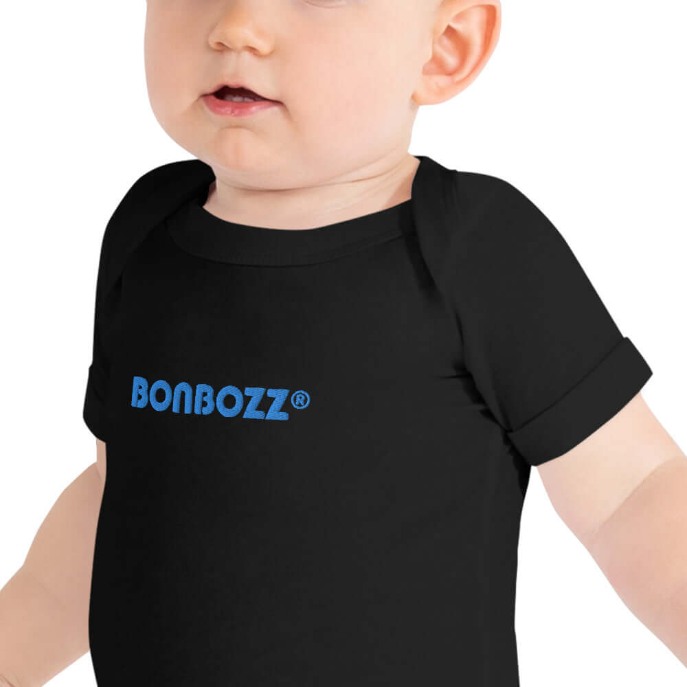 Baby wearing Kurzärmliger Baby-Einteiler N°0, black with blue logo, made from 100% combed cotton, features envelope neckline and snap closures.