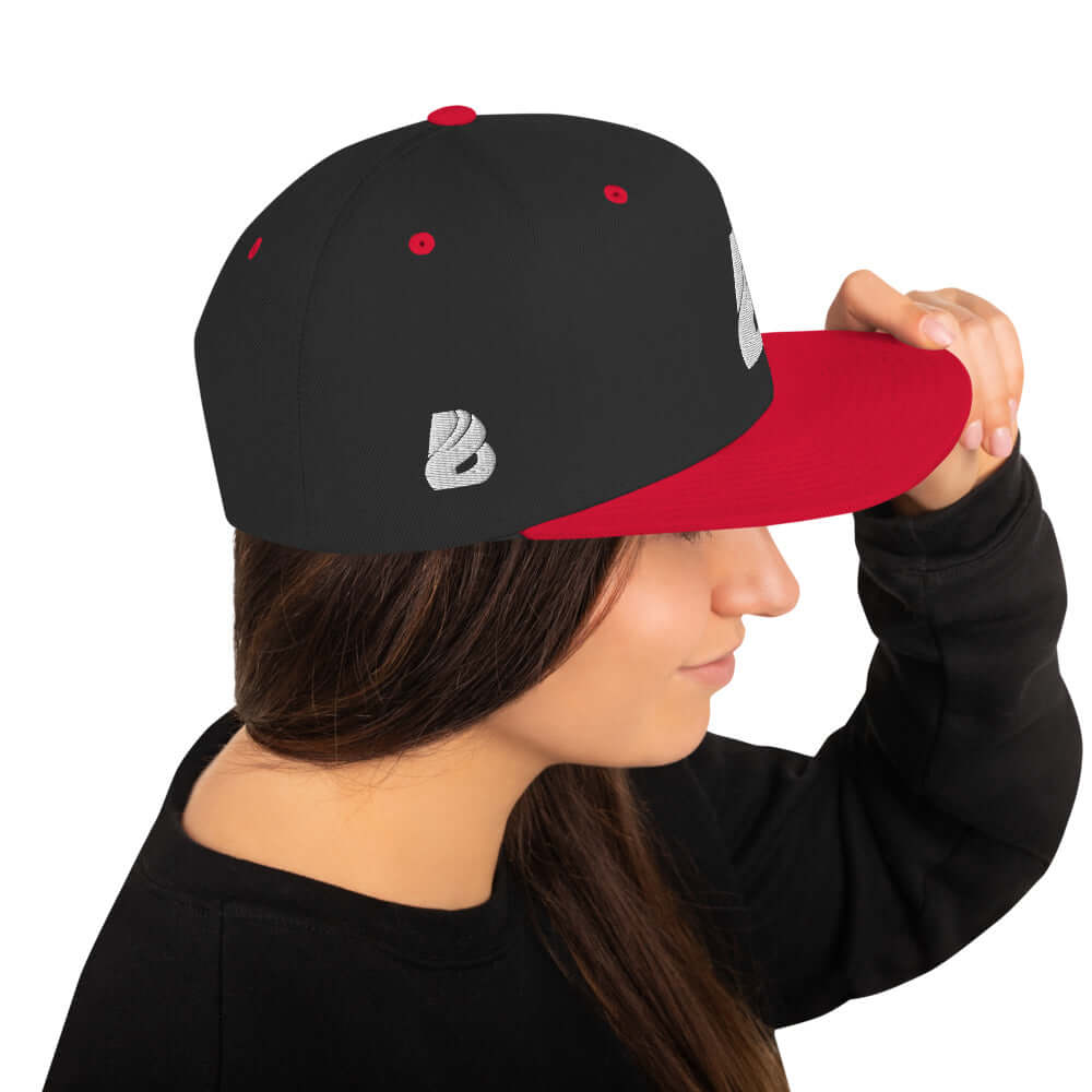 Snapback-Cap N°1 in black and red, worn by a woman, featuring classic fit and flat brim with adjustable snap closure.