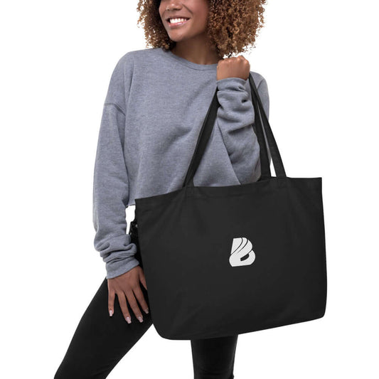 Person holding Großer Bio-Baumwollbeutel N°0, a large black organic cotton tote bag with logo, ideal for groceries, books, and travel.