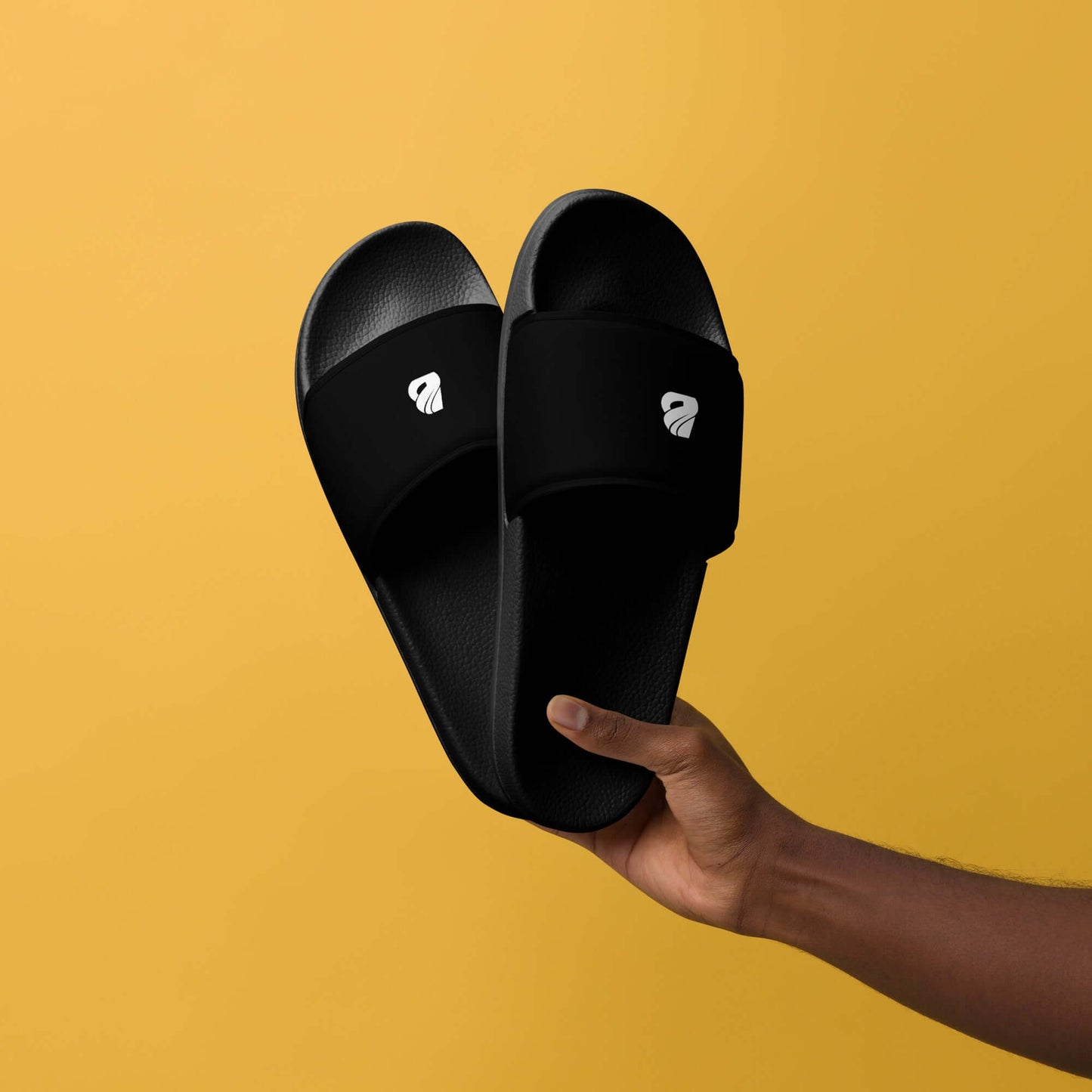 Herren-Schlappen N°1 black sandals with cushioned strap and contoured footbed, held against a yellow background