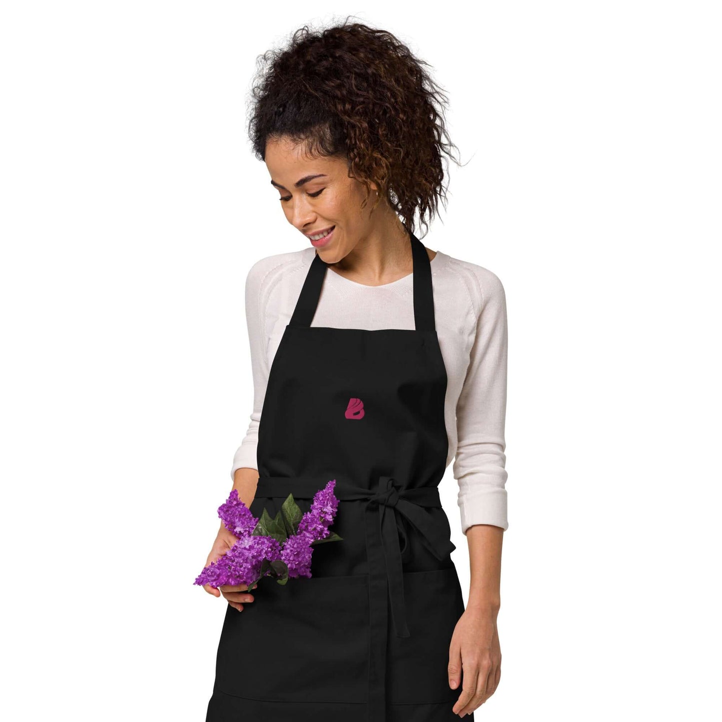 Person wearing Schürze aus Bio-Baumwolle N°0, holding purple flowers, showcasing stylish kitchen attire.