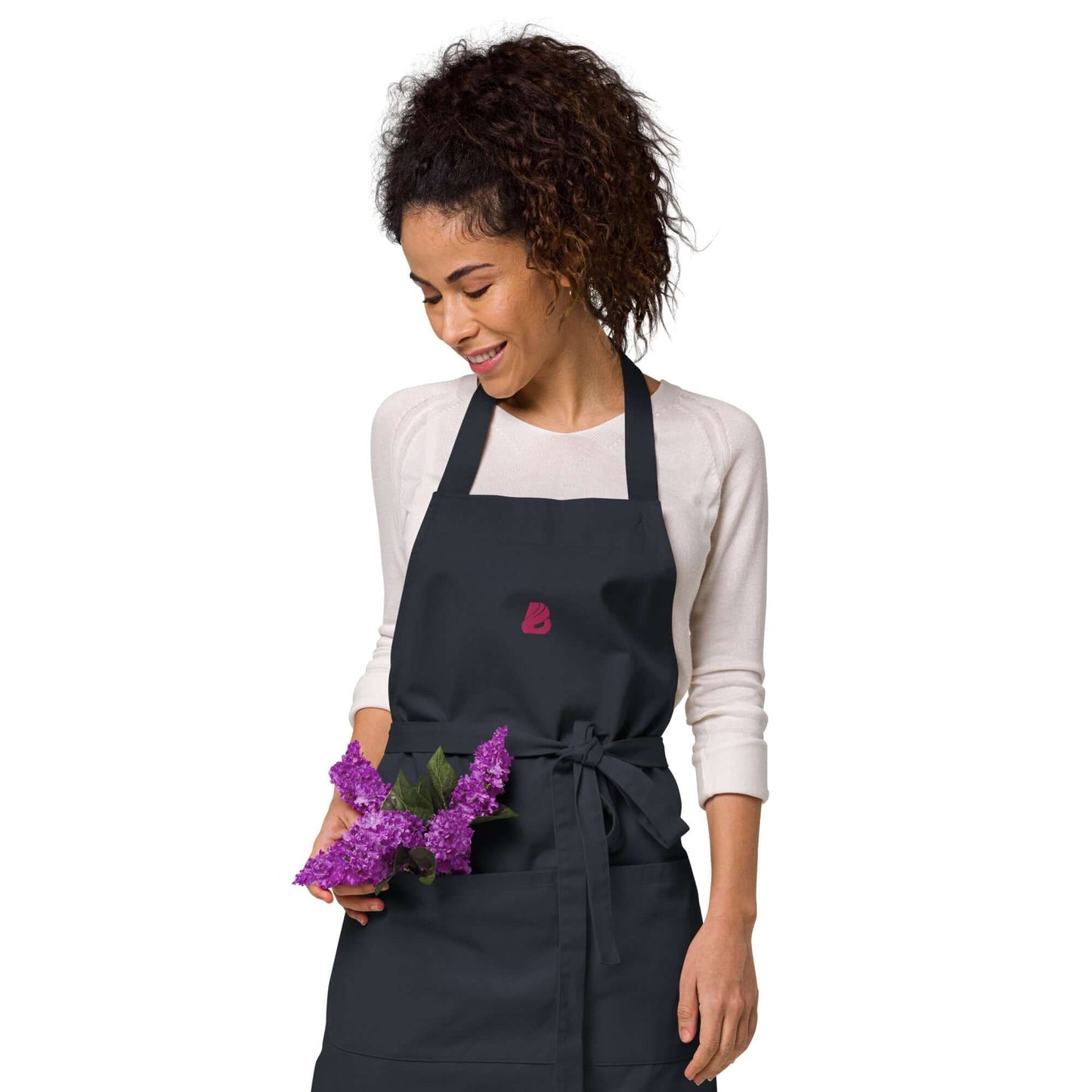 Frau trägt Schürze aus Bio-Baumwolle N°0, stilvoll in der Küche, 100 % Bio-Baumwolle, mit Blumen in der Hand.