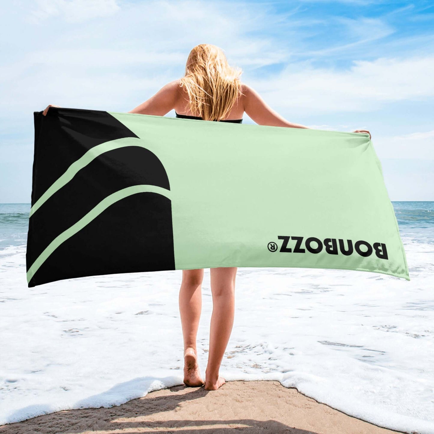 Woman holding Handtuch N°0 on beach with sea view, featuring vibrant design and water-absorbent terry fabric. Perfect for coastal relaxation.