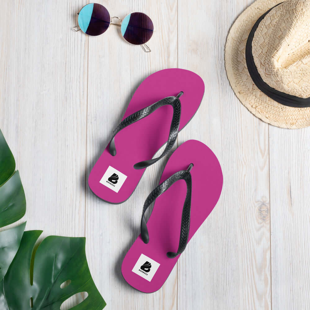 Pink Flip-Flops N°3 with black Y-shaped straps on a light wooden floor, summer accessories including sunglasses and sun hat