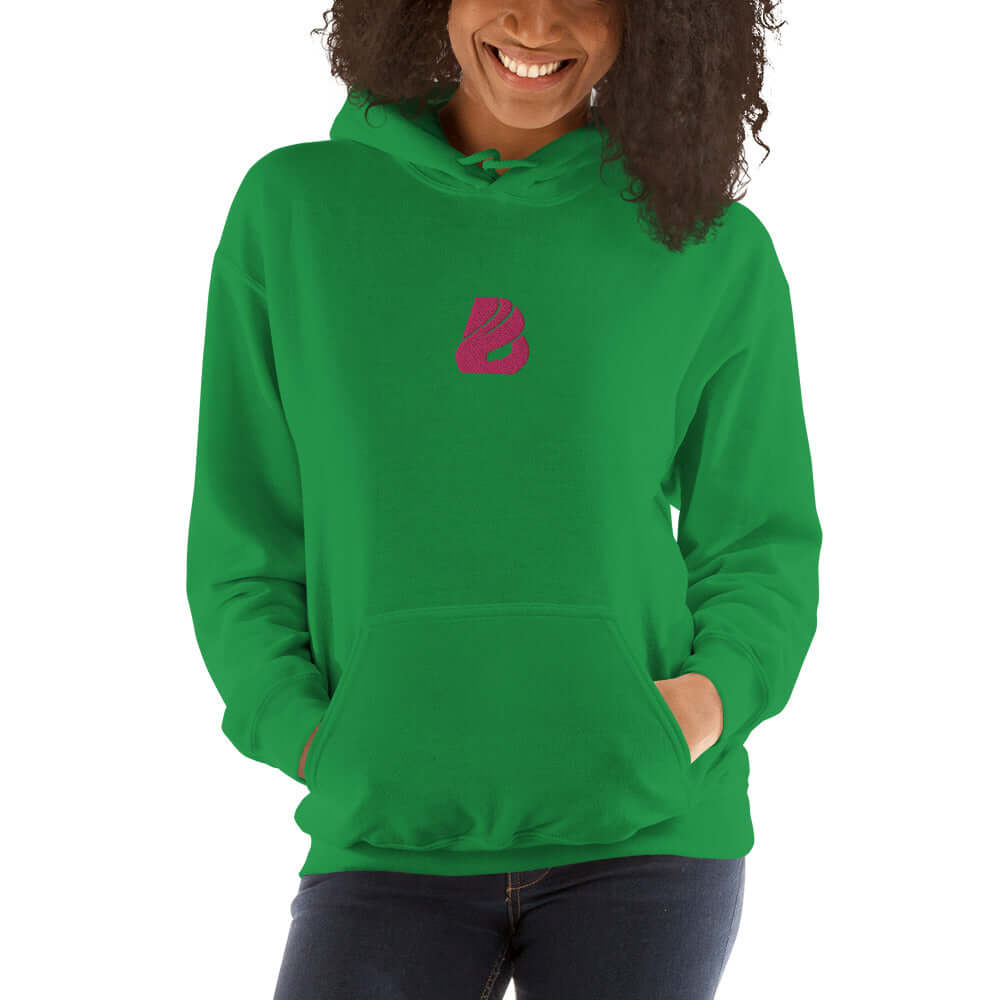 Woman wearing green Unisex-Kapuzenpullover N°44 with pink logo, cozy and stylish hoodie perfect for cool evenings.