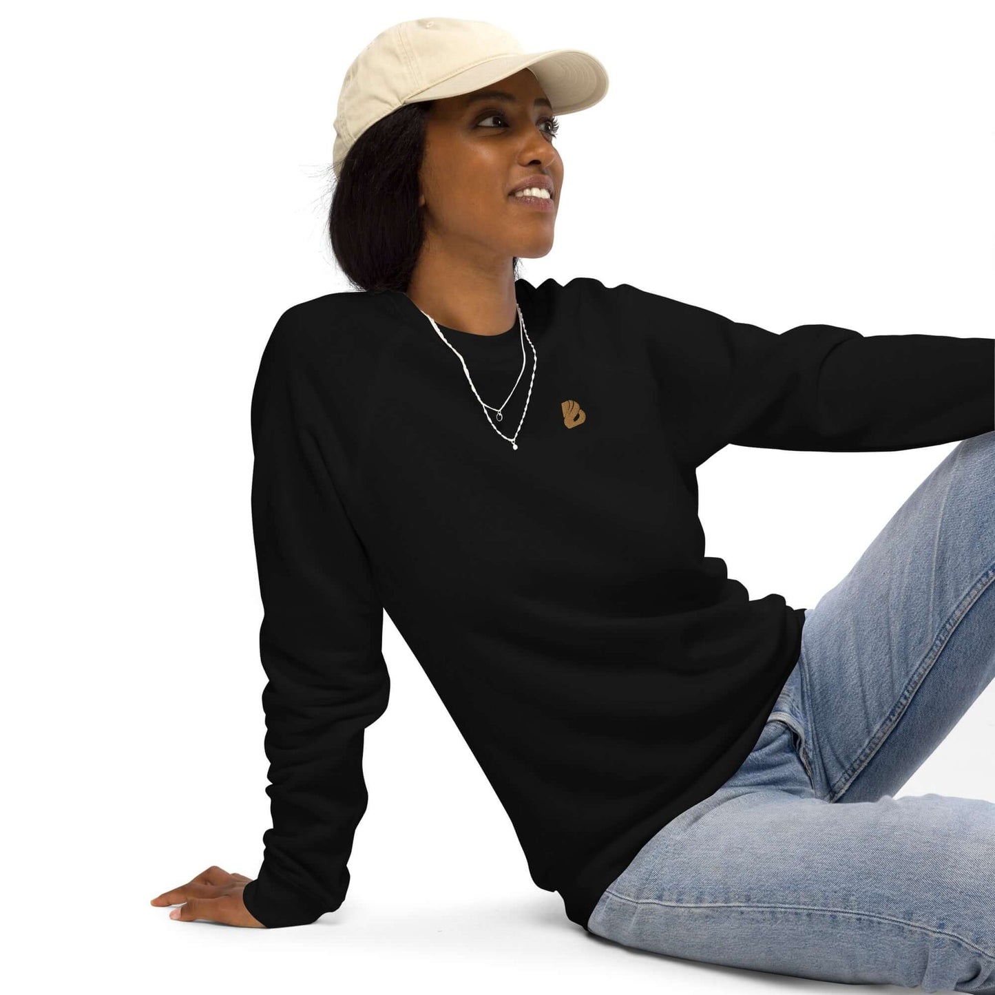 Person wearing Unisex Bio-Raglan-Pullover N°0, black with a relaxed fit, styled with a cap and jeans, showcasing comfort and style.